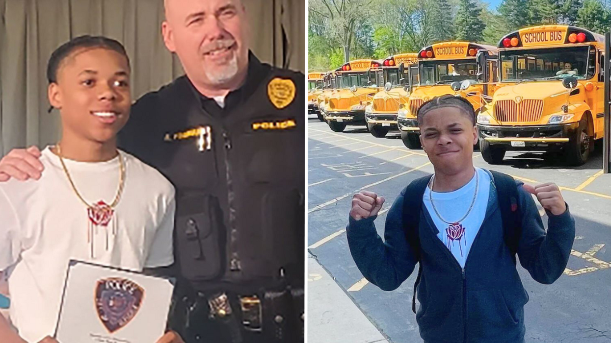 Police officer standing next to a teenager and a teen standing in front of a row of school buses.